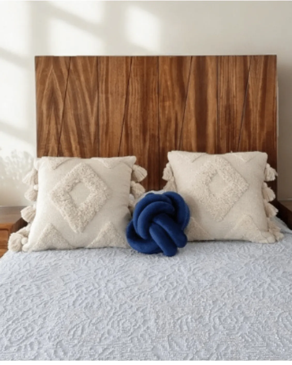 Wood headboard with diagonal grain, textured cushions and a blue knot pillow