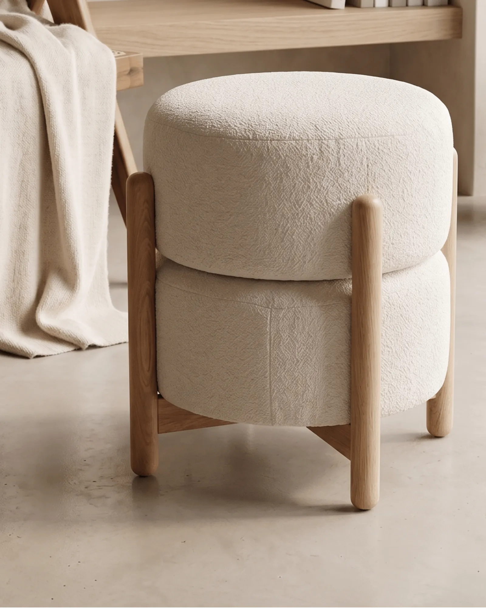 Boucle-upholstered ottoman on microcement floor, with throw blanket and clay vase